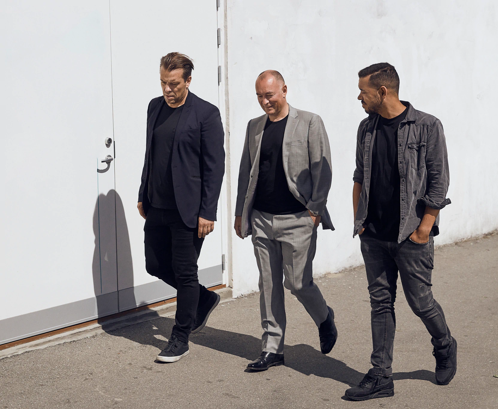 Three men in business attire walking confidently outdoors against a modern building, representing the Stella team or partners
